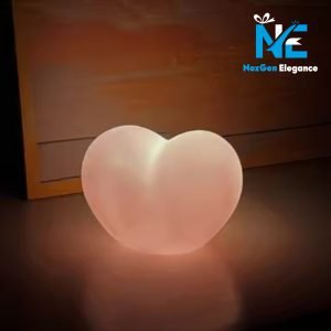 Glowing heart-shaped 3D lamp on a dark surface with soft warm light, frosted white finish, NexGen Elegance logo