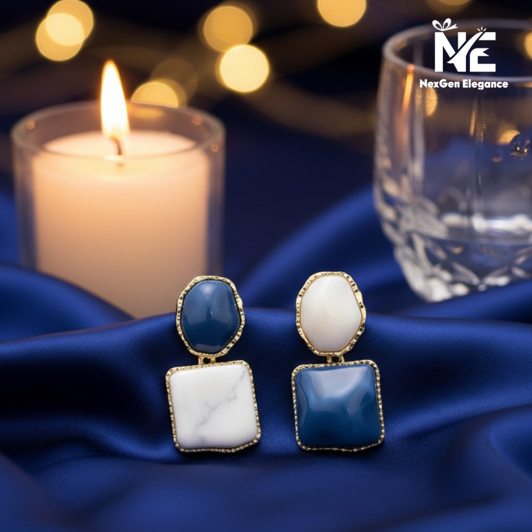Elegant dual tone stone earrings displayed on dark blue satin fabric with candlelight and crystal glass in background.